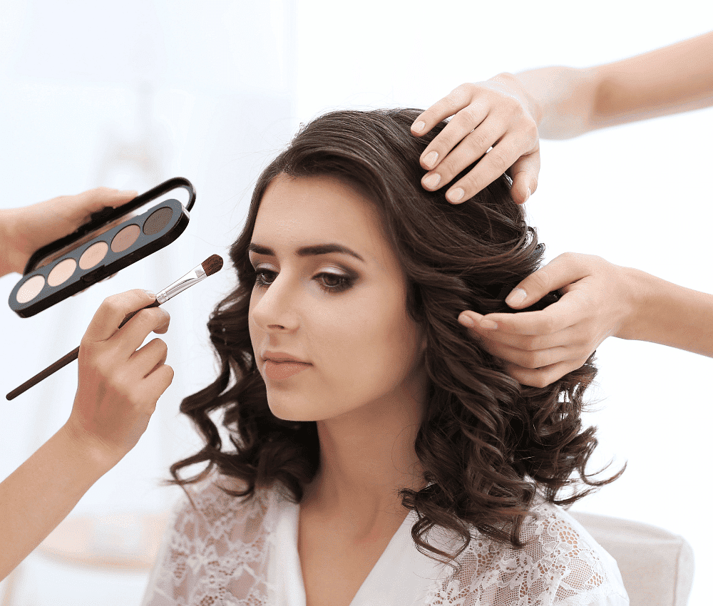 Woman getting makeup done while having hair styled.